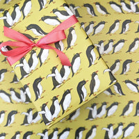 Gift box with penguin pattern and pink ribbon on a matching yellow background